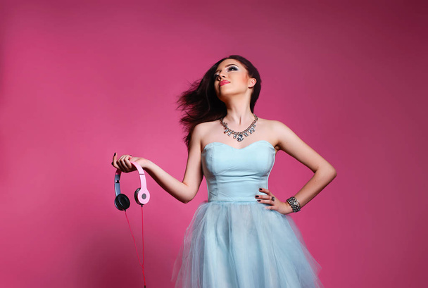 Fashion brunette over pink background. girl in a blue dress with headphones - Fotoğraf, Görsel
