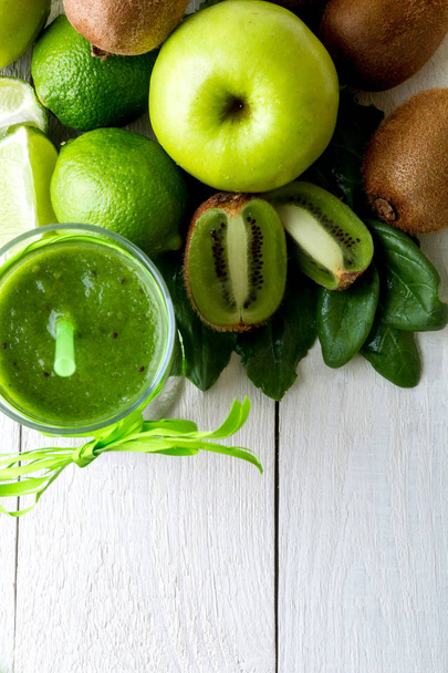 Green smoothie near ingredients for it on white wooden background. Apple, lime, spinach. Detox. Healthy drink. Top view. - Photo, image