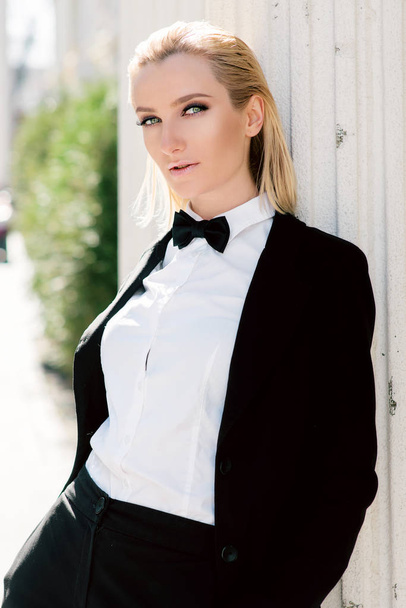 Portrait of stylish fashionable beautiful blonde woman in man black suit with bow tie outdoor - Photo, Image