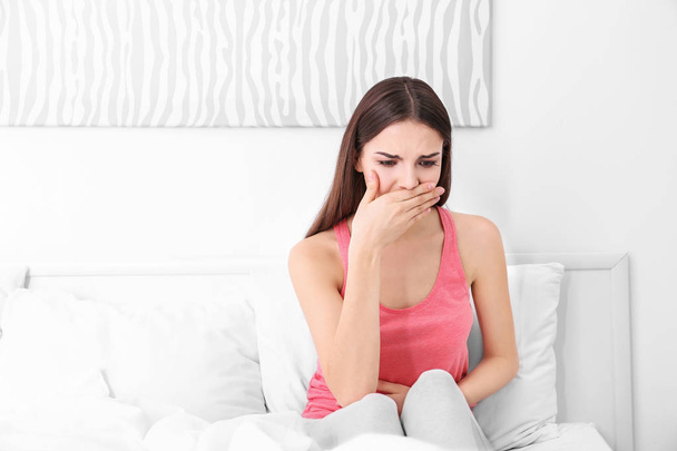 Young sick woman sitting on bed at home - Photo, image