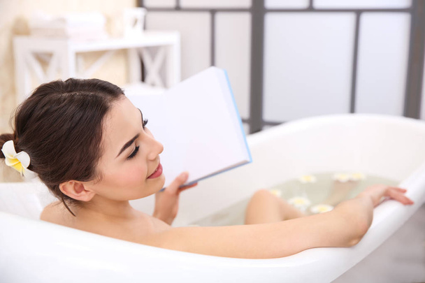Beautiful young woman reading book while taking bath at home - Foto, Bild