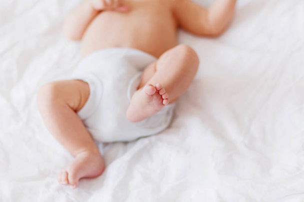 Baby's feet. Little child wearing white bodysuit and diaper. Cozy morning bedtime at home. - 写真・画像