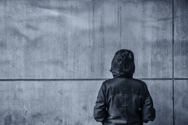 Unrecognizable hooded female person facing concrete wall as insu - Valokuva, kuva