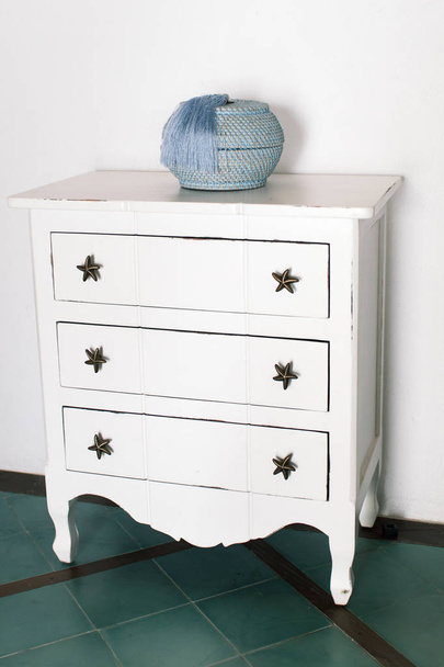 White vintage chest of drawers stands near white wall - Φωτογραφία, εικόνα