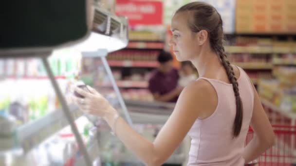 Young woman buying dairy food at the supermarket in the refrigerated section - Footage, Video