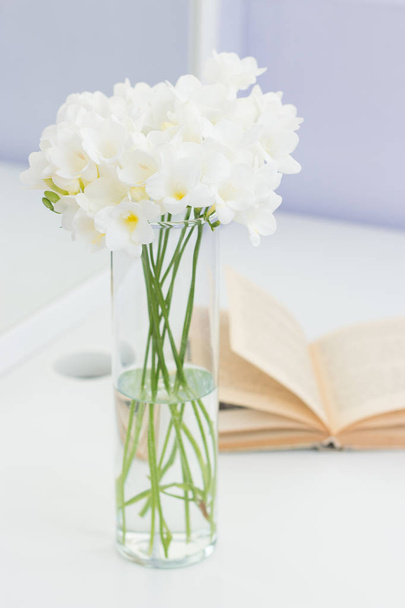 Kytice bílých květů do vázy umístěna na stůl. Útulný obrázek. Kytice bílých květů ve váze a knihu na bílém stole. - Fotografie, Obrázek