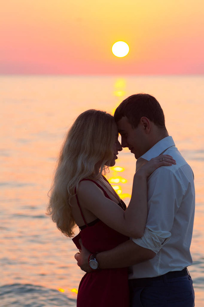 昇る太陽の光線で海辺に美しいロマンチックなカップル - 写真・画像