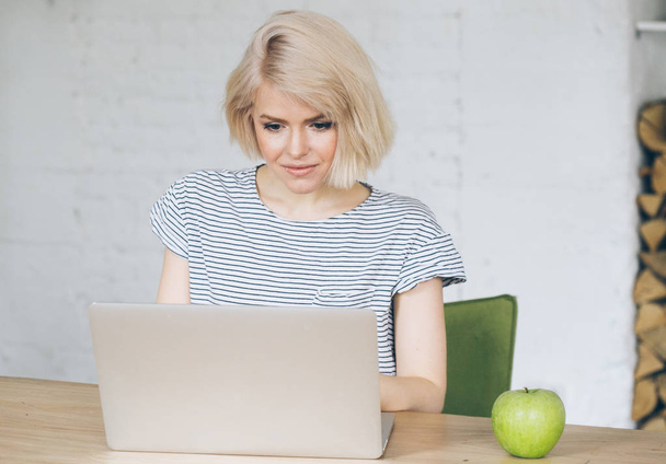 Beautiful young woman sits in front of a laptop. Apple beside her - Photo, Image