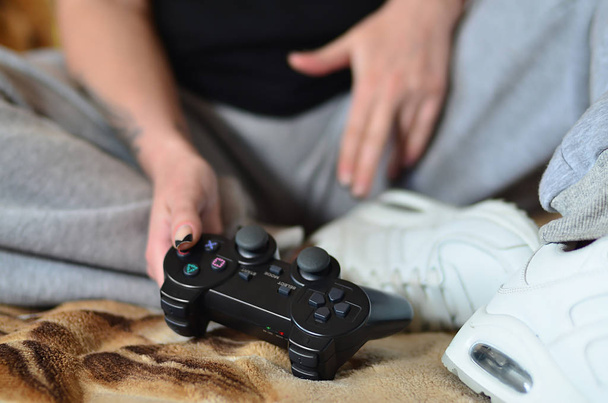 Una joven en pantalones grises sostiene un joystick de juego moderno negro con muchos botones para administrar videojuegos. El concepto de ocio juvenil a través de videojuegos
 - Foto, imagen