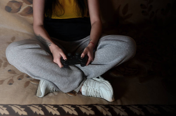 ein junges Mädchen in grauer Hose hält einen schwarzen modernen Spielsteuerknüppel mit vielen Knöpfen zur Steuerung von Videospielen in der Hand. das Konzept der Jugendfreizeit durch Videospiele - Foto, Bild