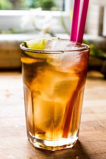 Long island iced tea cocktail with lime, ice and served with pink straw - Foto, imagen