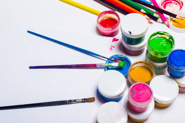 Gouache-verf, penselen en kleurpotloden op een lichte achtergrond - Foto, afbeelding