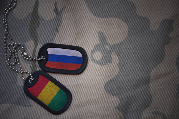 Army blank, dog tag with flag of russia and guinea on the khaki texture background. военная концепция
 - Фото, изображение