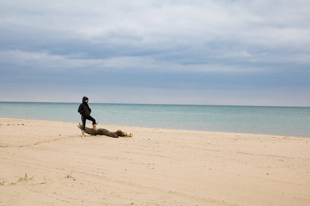 Kobieta stojąc na plaży w pobliżu stary dziennik. Wody morskiej zieleni, burzowe na tle - Zdjęcie, obraz