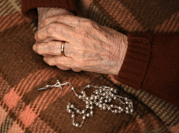 Primer plano de la anciana rezando con rosario de plata con cruz
 - Foto, Imagen
