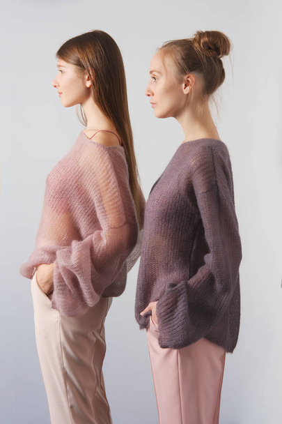 Two pretty girls in thin angora sweater and pants posing near the wall - Foto, afbeelding