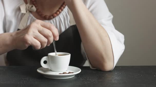 Γυναίκα στην ποδιά ανακατέψτε τη ζάχαρη σε μικρό φλιτζάνι ζεστό καφέ. - Πλάνα, βίντεο