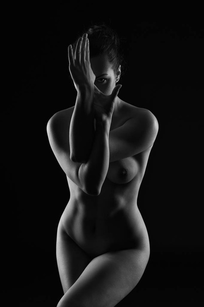 Art nude, perfect naked body, sexy young woman on dark background, black and white studio shot - Foto, Imagem