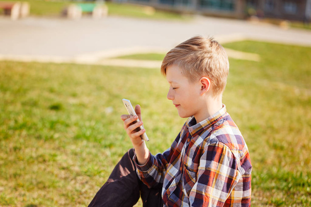 Child playing phone outdoors in sunny day. - Фото, изображение