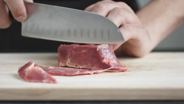На переднем плане молодой шеф-повар разрезал тонкие куски мяса ножом на доске
. - Кадры, видео