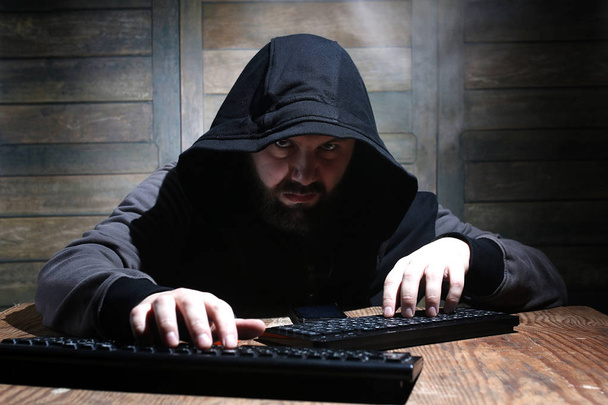 хакер в черном капюшоне в комнате с деревянными стенами
 - Фото, изображение