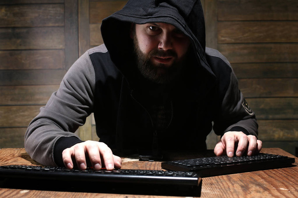 хакер в черном капюшоне в комнате с деревянными стенами
 - Фото, изображение