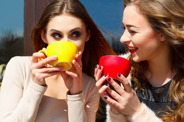 Two young pretty woman laughing outdoors and drinking coffee or  - Фото, зображення