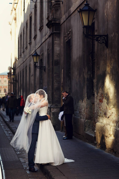 Newlyweds kiss under a veil standing on the old street - Фото, зображення