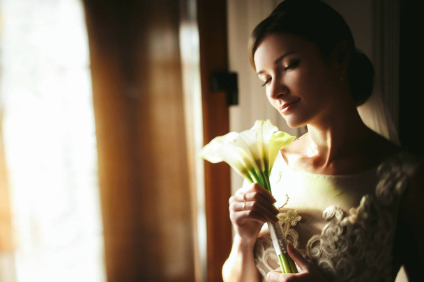 Bride holds a tender bouquet of callas behind her face  - Foto, Bild