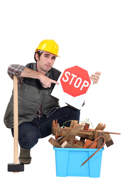 Labourer holding a stop sign while squatting before a bin full of wood - Zdjęcie, obraz