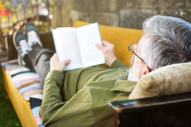 Älterer Mann liest auf Bett im Hof - Foto, Bild