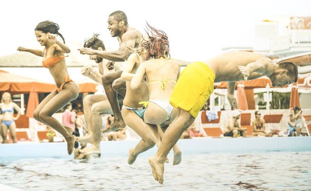 Vue latérale d'amis multiraciaux sautant à la fête de la piscine - Concept de vacances avec des gars et des filles heureux de s'amuser dans la journée d'été à aquapark loisirs - Les jeunes actifs sur filtre de contraste rétro
 - Photo, image