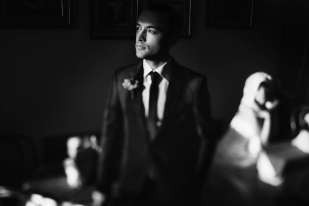 Gorgeous groom looks up at the sun through the cafe window  - 写真・画像