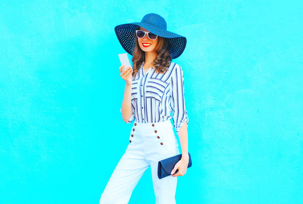 Fashion young woman is using a smartphone wearing a straw hat, w - Фото, зображення