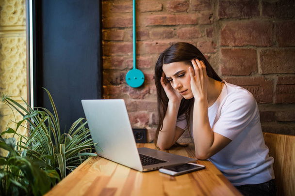 Шокированная и грустная женщина держит в руках компьютер, ноутбук планшетный экран выглядит удивленным в кафе
 - Фото, изображение
