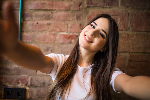 schöne junge Frau macht Selfie auf einem Smartphone auf einer Ziegelwand Hintergrund - Foto, Bild