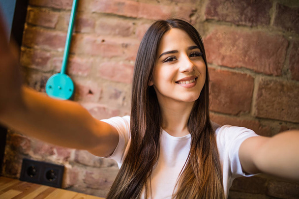 Bella giovane donna che fa selfie su uno smartphone su uno sfondo muro di mattoni
 - Foto, immagini