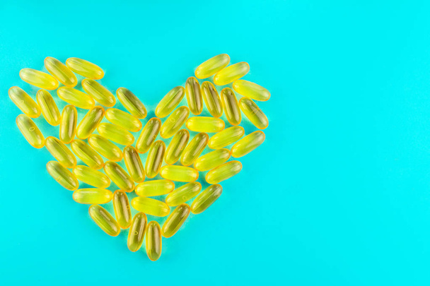 Bir sürü sarı kapsül omega 3, yağ asidi, mavi arka planda kalp şeklinde balık yağı. - Fotoğraf, Görsel