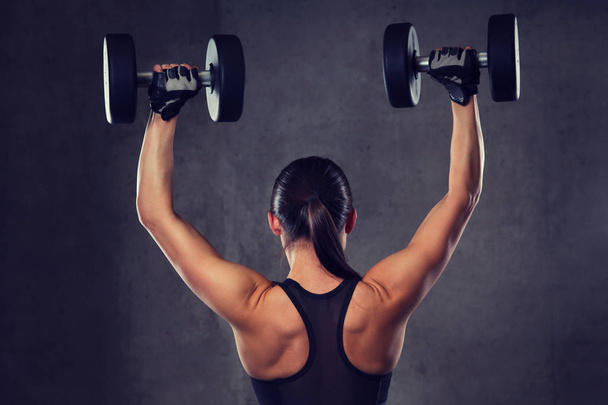 young woman flexing muscles with dumbbells in gym - Foto, Imagen