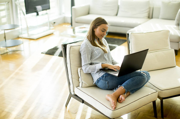 Nainen käyttää kannettavaa tietokonetta sohvalla huoneessa
 - Valokuva, kuva