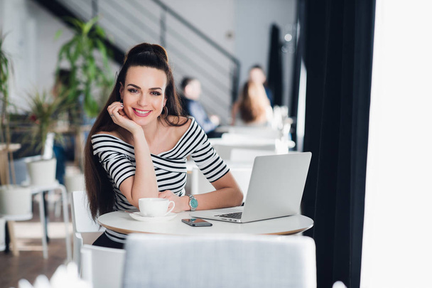 Foto van gelukkig lachende vrouw met laptop in een cafe en kijken naar de camera. - Foto, afbeelding