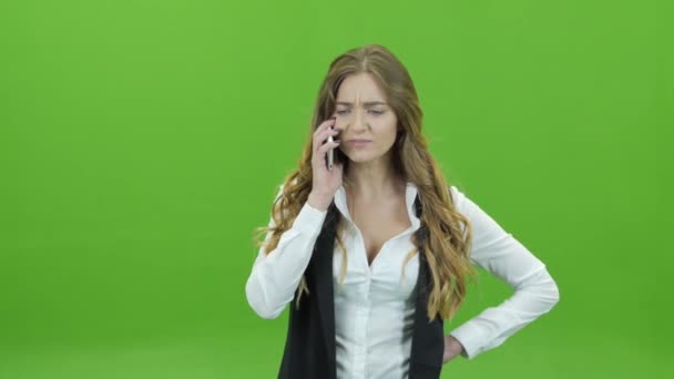 A young girl on a green background with displeasure on the phone - Felvétel, videó