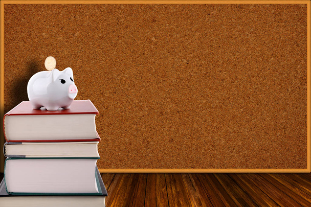 Piggy Bank on Stack of Books and Corkboard Background - Photo, Image