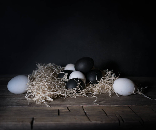 Easter. Easter night. Black and White eggs, feathers on a wooden table. Vintage. Dark background - Foto, Imagem