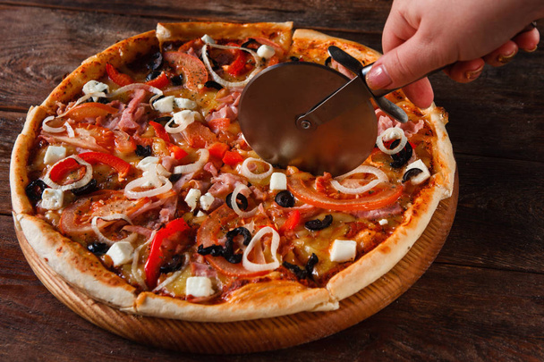 Hand cutting fresh tasty pizza. Italian cuisine. - Photo, Image