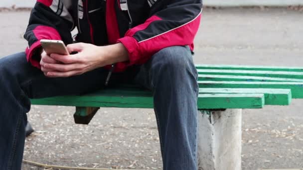 Osamělý muž sedí v parku na lavičce psát něco na smartphone - Záběry, video