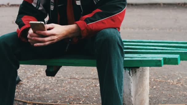 osamělý v červené sako je posezení v parku a cosi psal na smartphone - Záběry, video