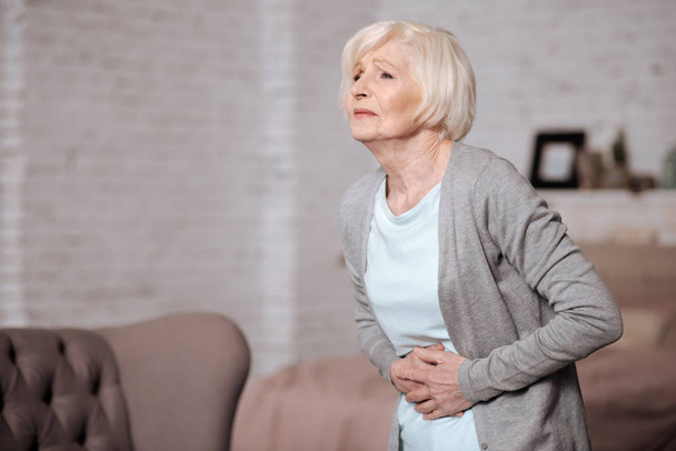 Aged woman standing with stomachache - Zdjęcie, obraz