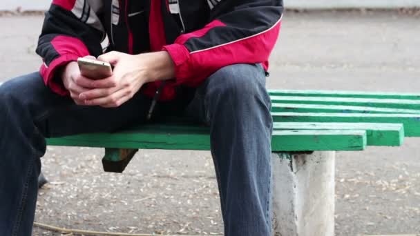 Egy magányos ember ül a parkban egy padon, gépelés valamit a smartphone - Felvétel, videó