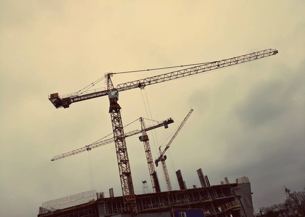 Three building cranes against the background of a rainy gray sky - Photo, Image